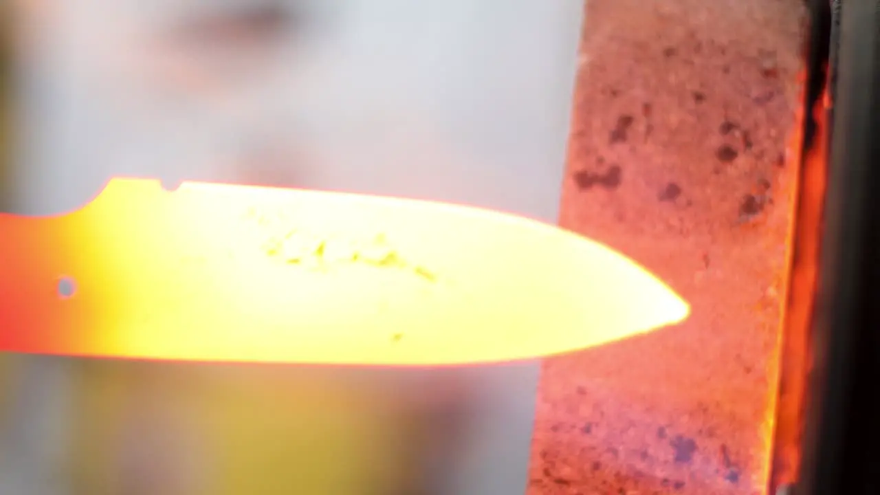 burning red hot Knife being removed from oven ready to be forged with fire flames escaping from the hot oven entrance with blurred background