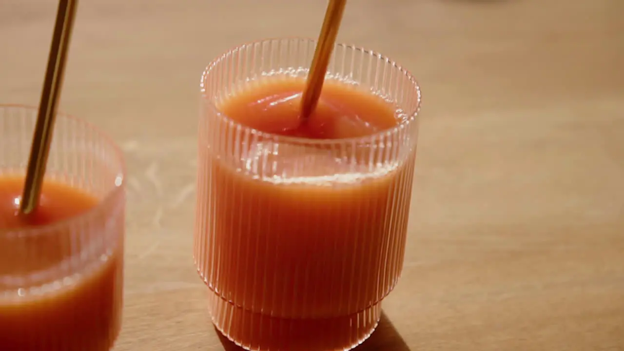 A Orange Cold Pressed Juice gets stirred with a metal straw in a drinking glass during Detox Cleanse Slow Motion