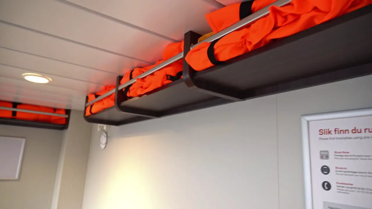 Lifejackets stored in shelves over seats onboard passenger ship Camera looking straight at closest shelf before panning left and revealing passenger area