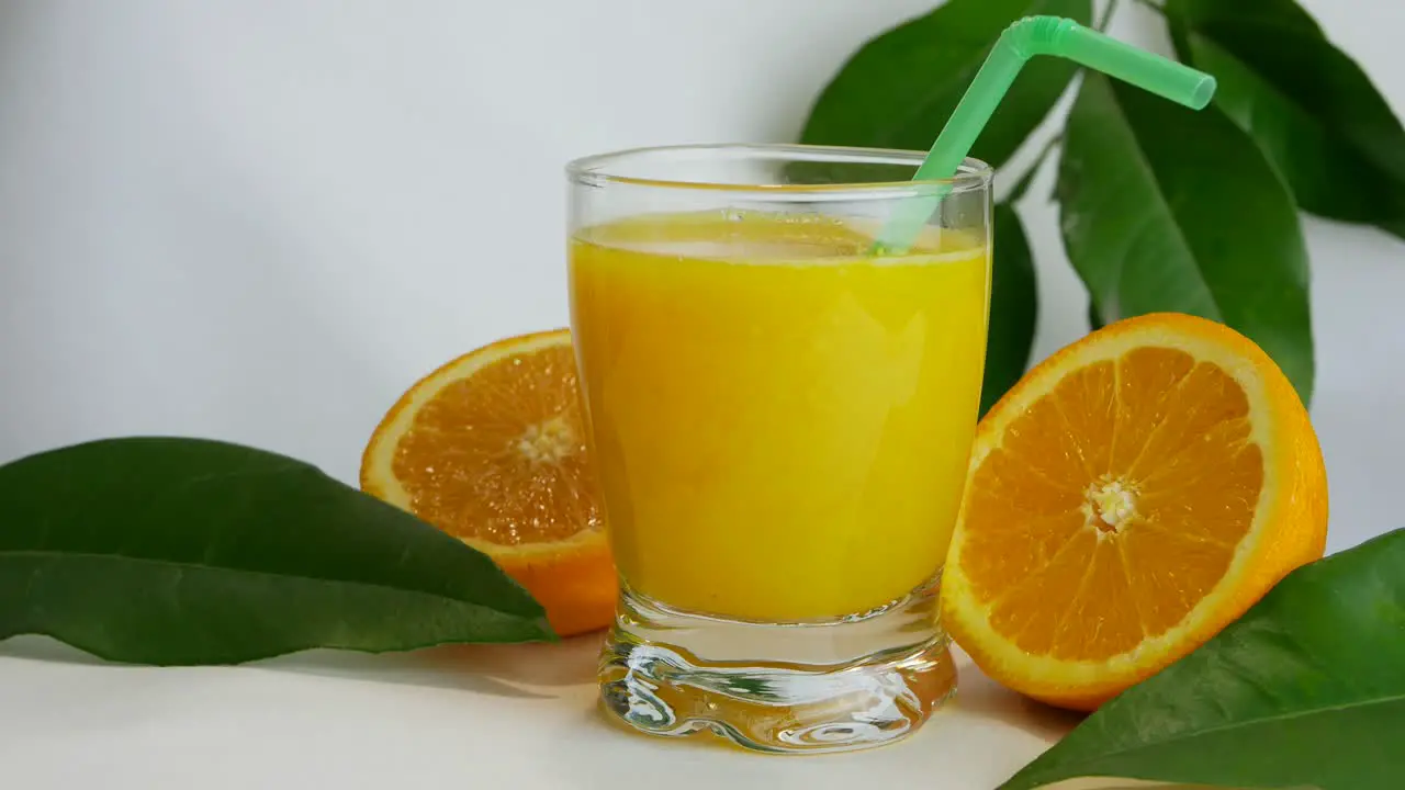 Close up studio shot of full glass of orange juice and orange halves slow pan