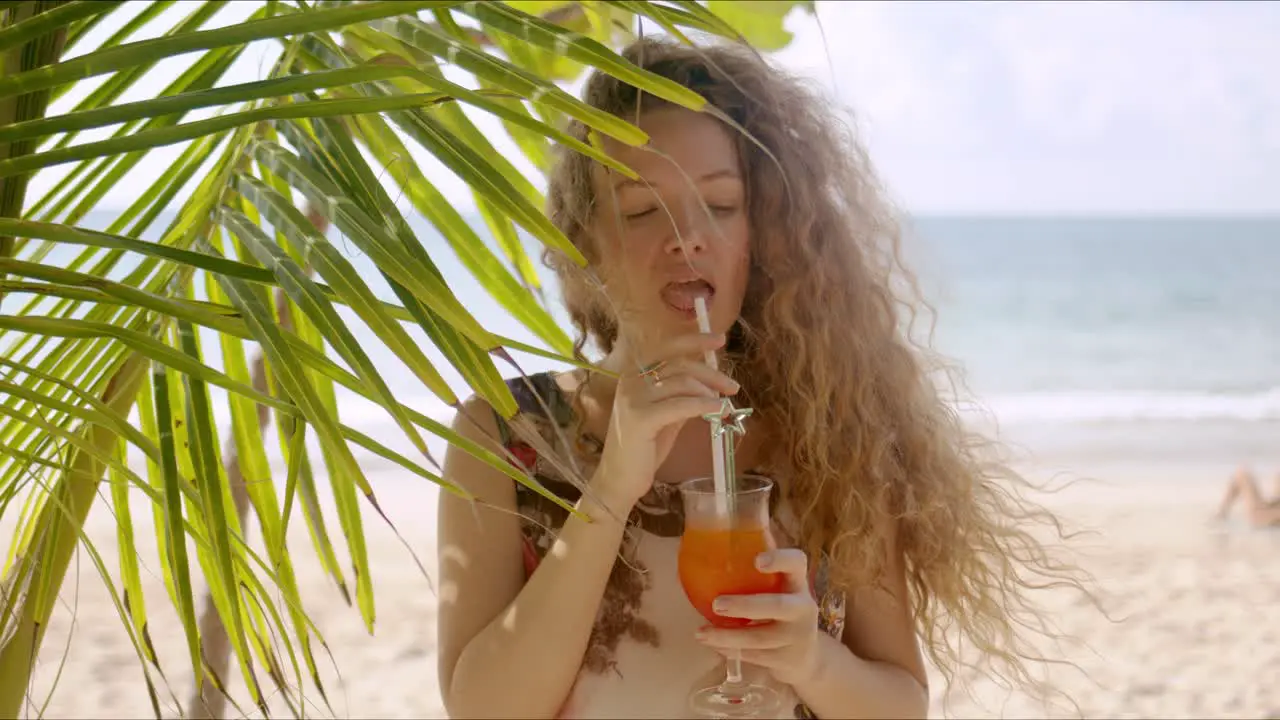 Attractive female drinking beverage beside palm tree