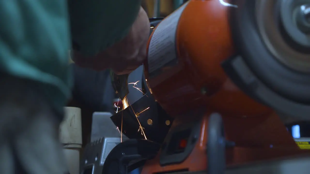 A static low angle shot of a mechanic polishing a welded metallic car piece with sparks flying down his spinning polishing wheel