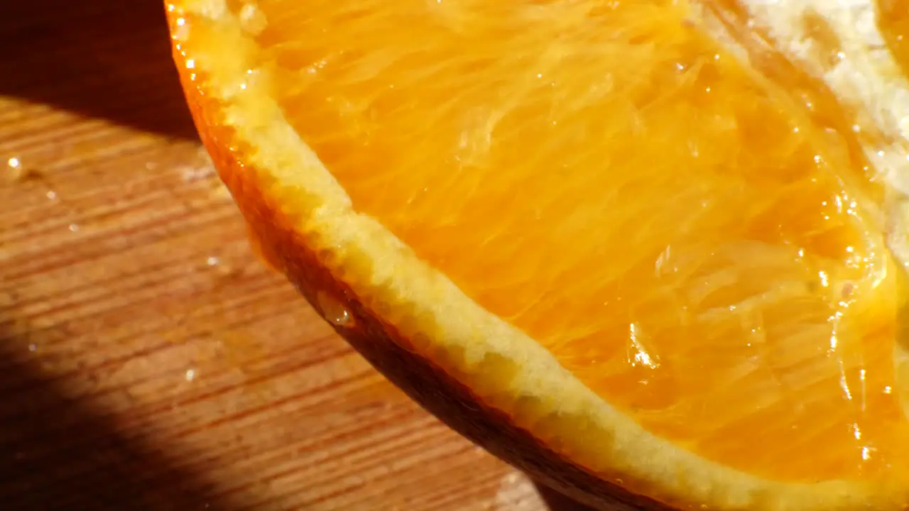 Macro shot on a ripe orange fruit slice with juice dripping off of it in the sunlight on a cutting board for a healthy snack