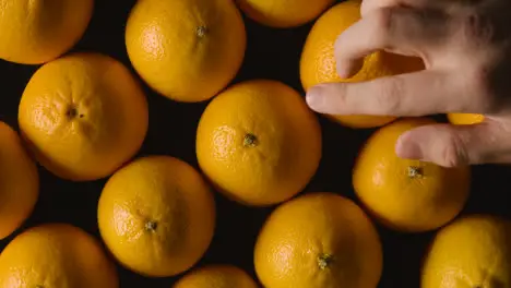 Overhead Studio Shot Of Hand Choosing From Oranges Revolving Against Black Background 