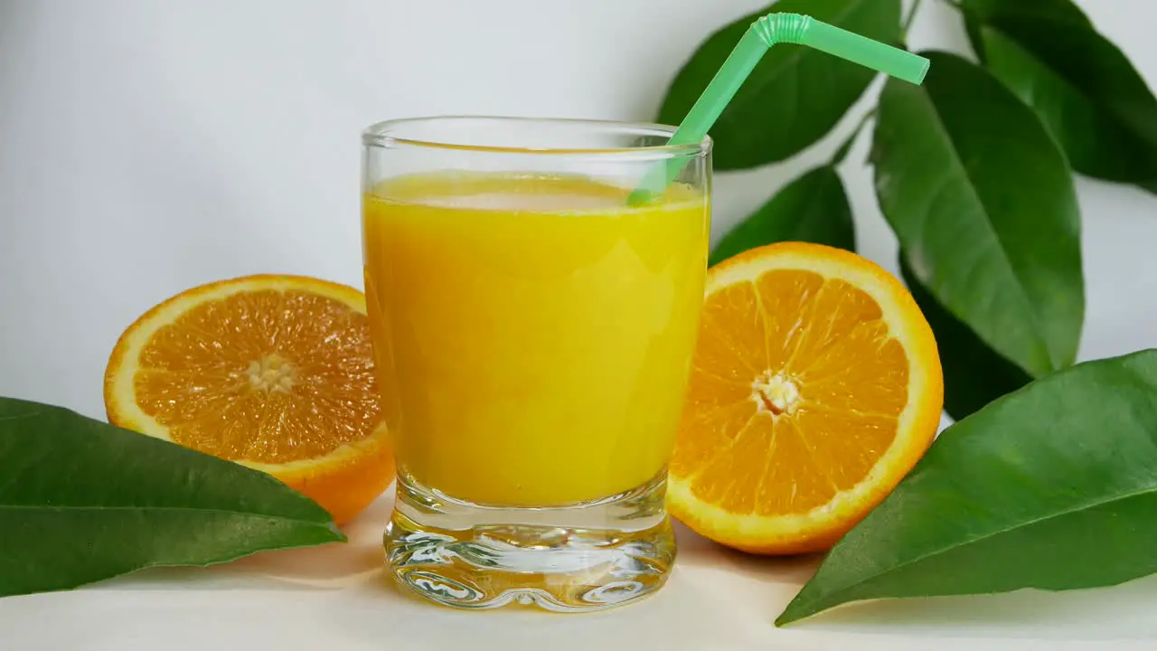 Close up studio shot of full glass of orange juice and orange halves fast pan