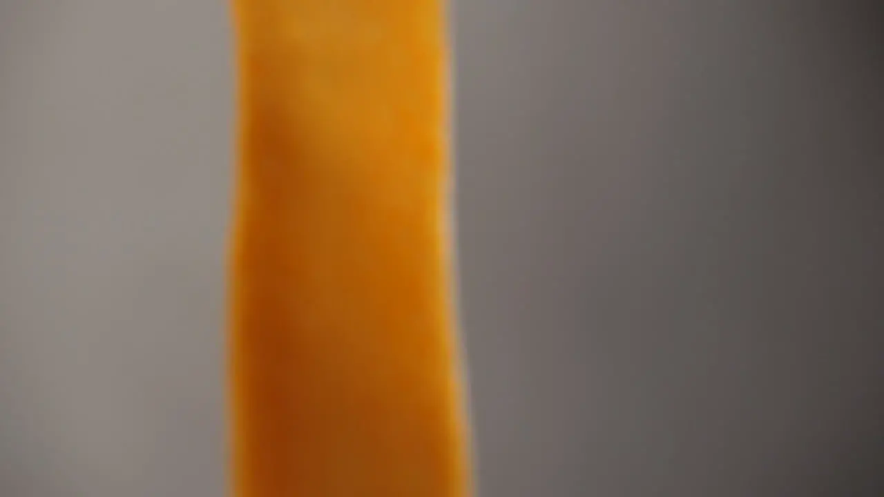 Close-up of a very thin strip of orange sweet potato moving in front of the camera in slow motion shot