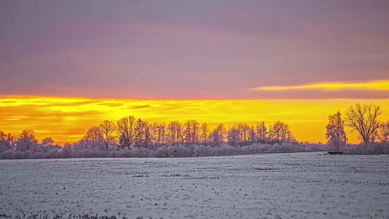 Orange clouds in golden sky over snowy landscape with trees in a winter time-lapse