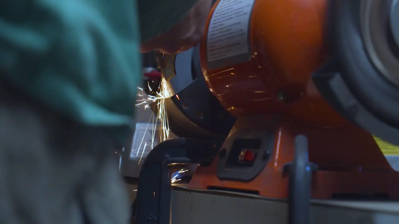 A moving low angle shot of a mechanic polishing a welded metallic car piece with sparks flying down his spinning polishing wheel