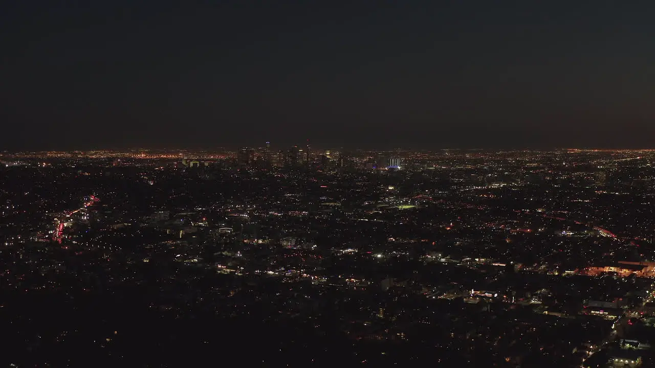 AERIAL Slow flight over Hollywood Hills at Night with view on Downtown Los Angeles Skyline