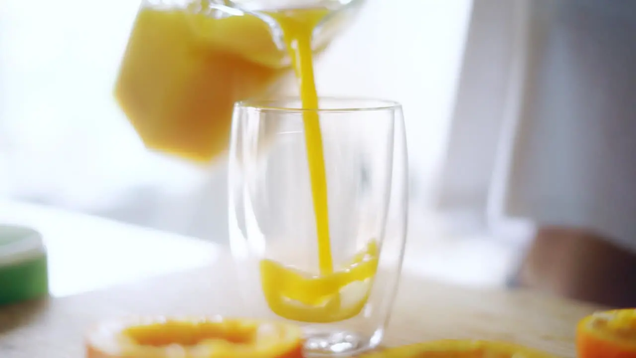 Woman pouring orange juice from glass jar into glass Close up glass