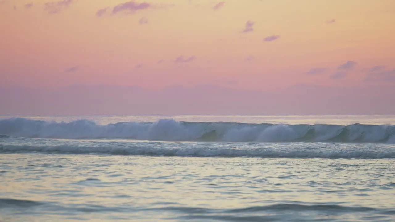 A surfers silhouette amid large rolling waves and a burnt orange sunset