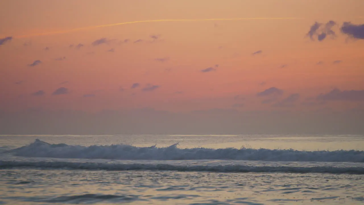 A fiery orange sunset with waves rolling in and the silhouette of a surfer