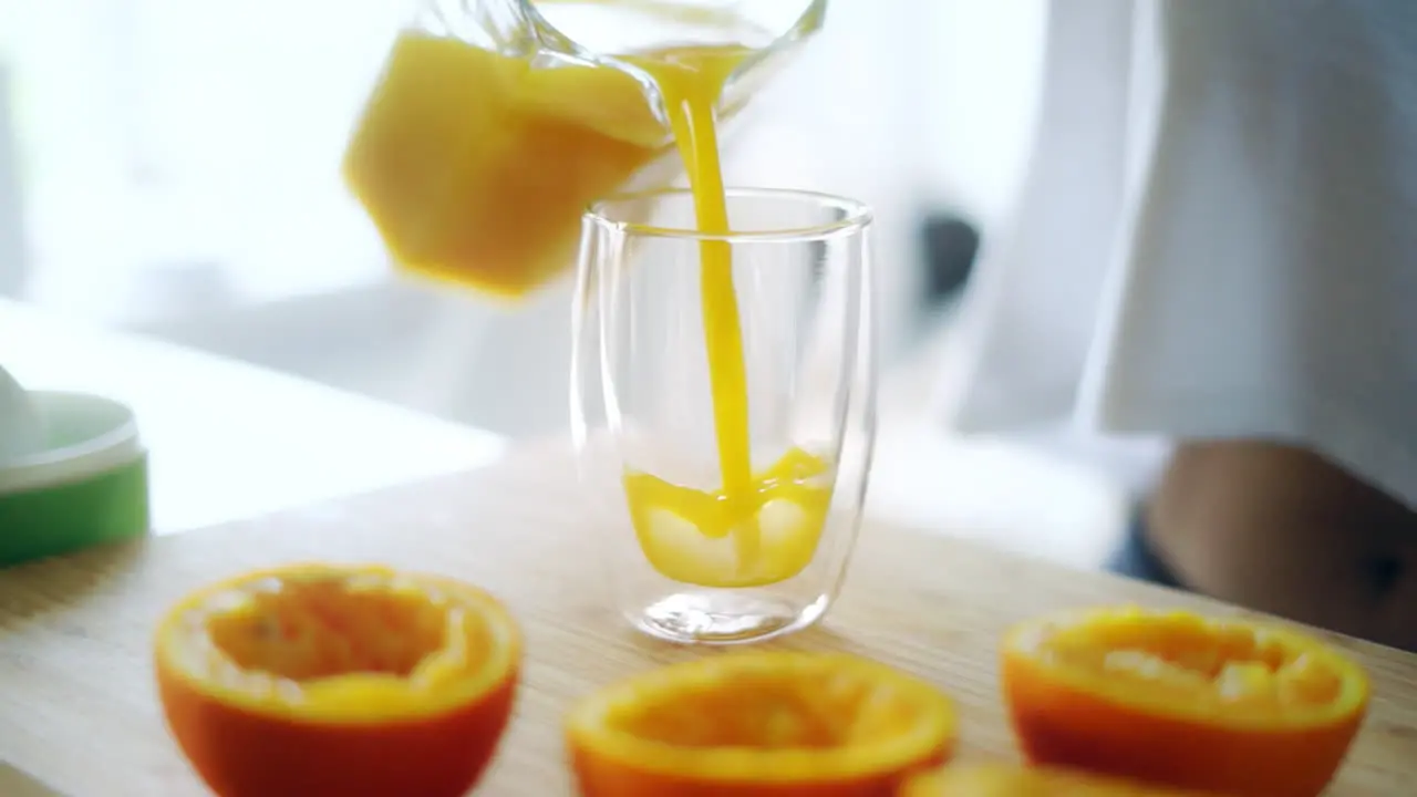 Pouring fresh orange juice from glass jar into glass Squeezed orange parts