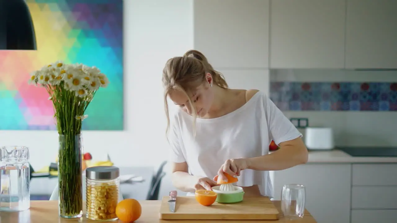 Young woman squeezing fresh orange juice with citrus squeezer