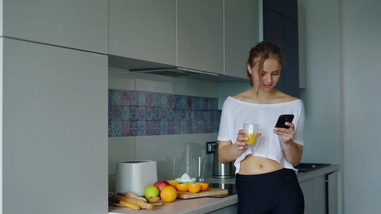 Beautiful girl drinking fresh orange juice from glass Woman using smartphone