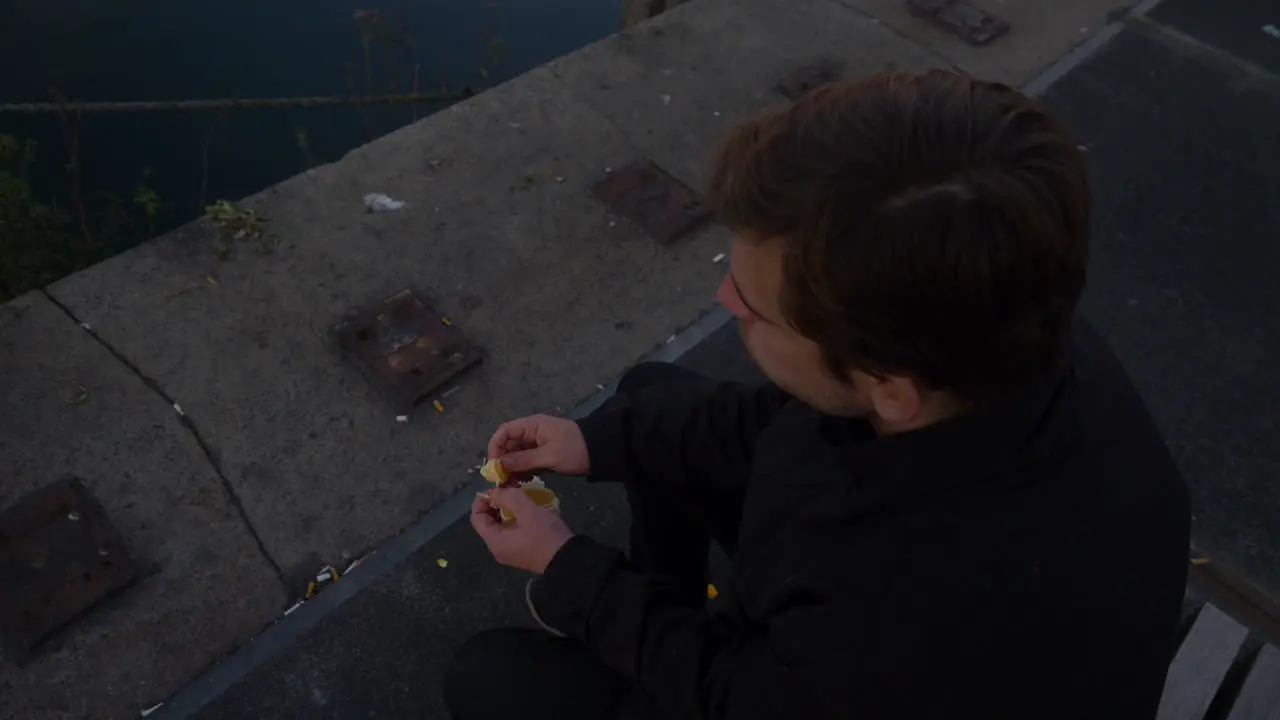 Top down overhead close up of a young man sitting on a bench and eating orange slices