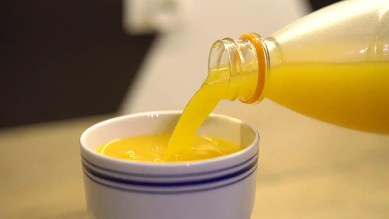 Pouring orange juice from plastic bottle into a white coffee cup with blue stripes