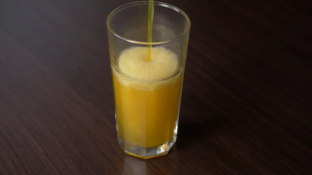 Pouring sparkling orange soda into tall glass on a wooden table