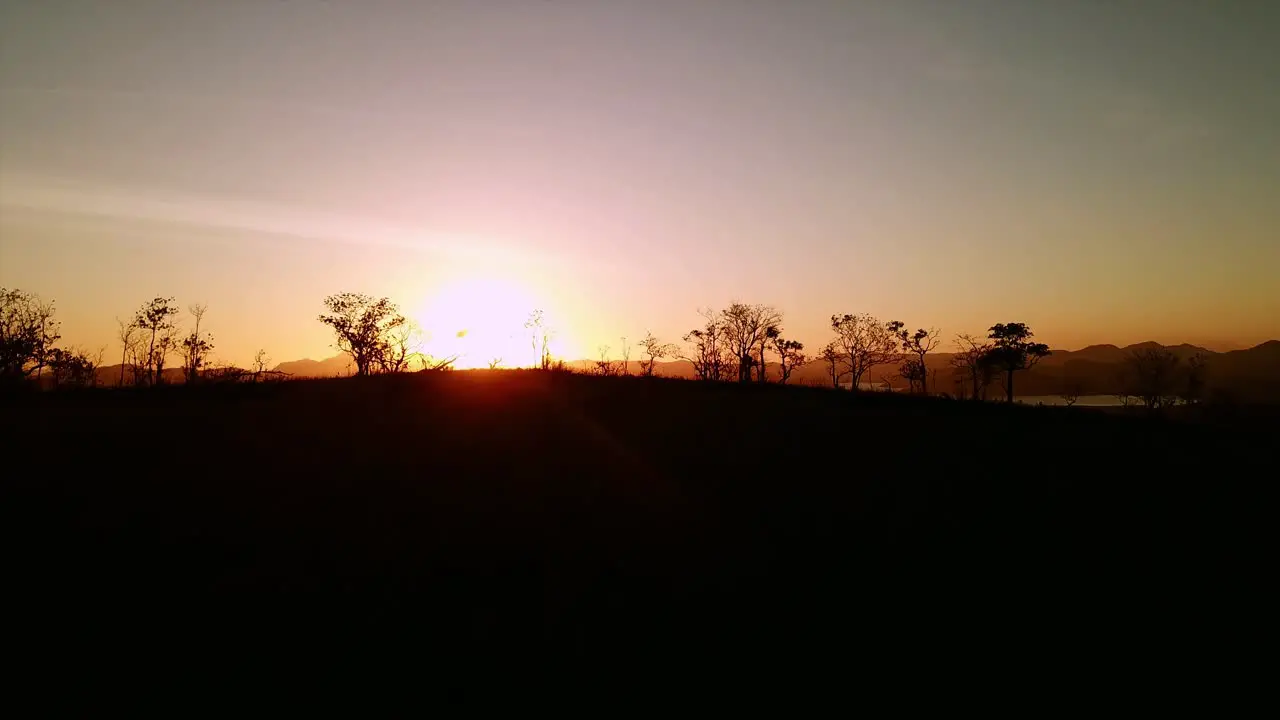 Aerial drone shot of dramatic sunset flying above silhouette of trees and hills