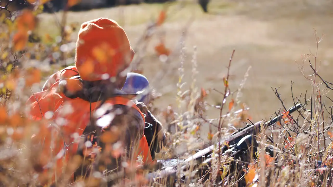 Elk Hunter looks in to distance with binoculars while laying on ground