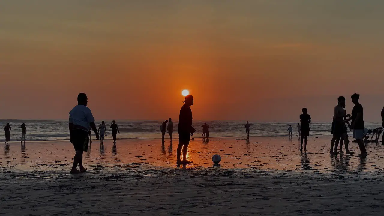 Burnt orange golden sunset on beach as men play barefoot soccer