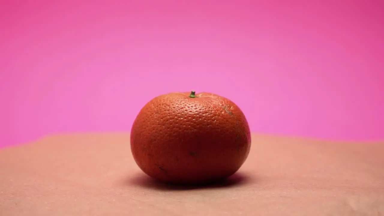 Ripe mandarine rotate on pink and old paper background 4k video colorized