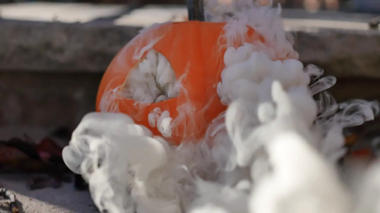 Grey smoke coming out of a jack-o-lantern sitting on steps atop dead fall leaves