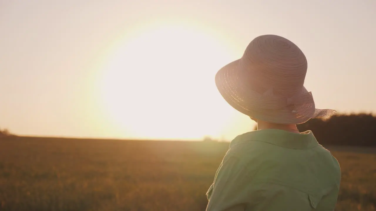 A Female Farmer In A Hat Looks At The Horizon Above A Field Of Wheat Enjoying The Sunset The Back Vi