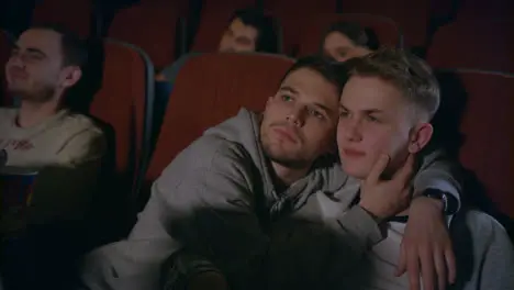 Couple gays embracing in movie theater Homosexual men embrace in movie theatre