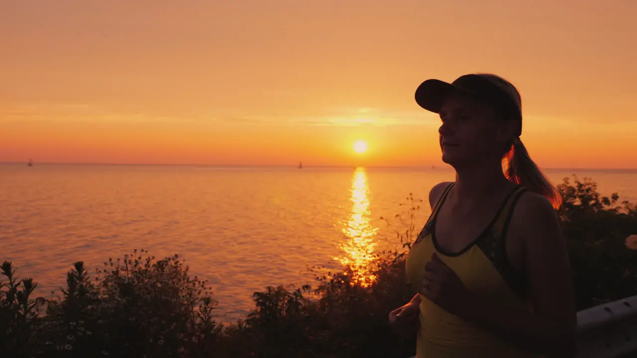 A Young Woman Runs In A Picturesque Place By The Sea Where The Sun Sets Over The Water