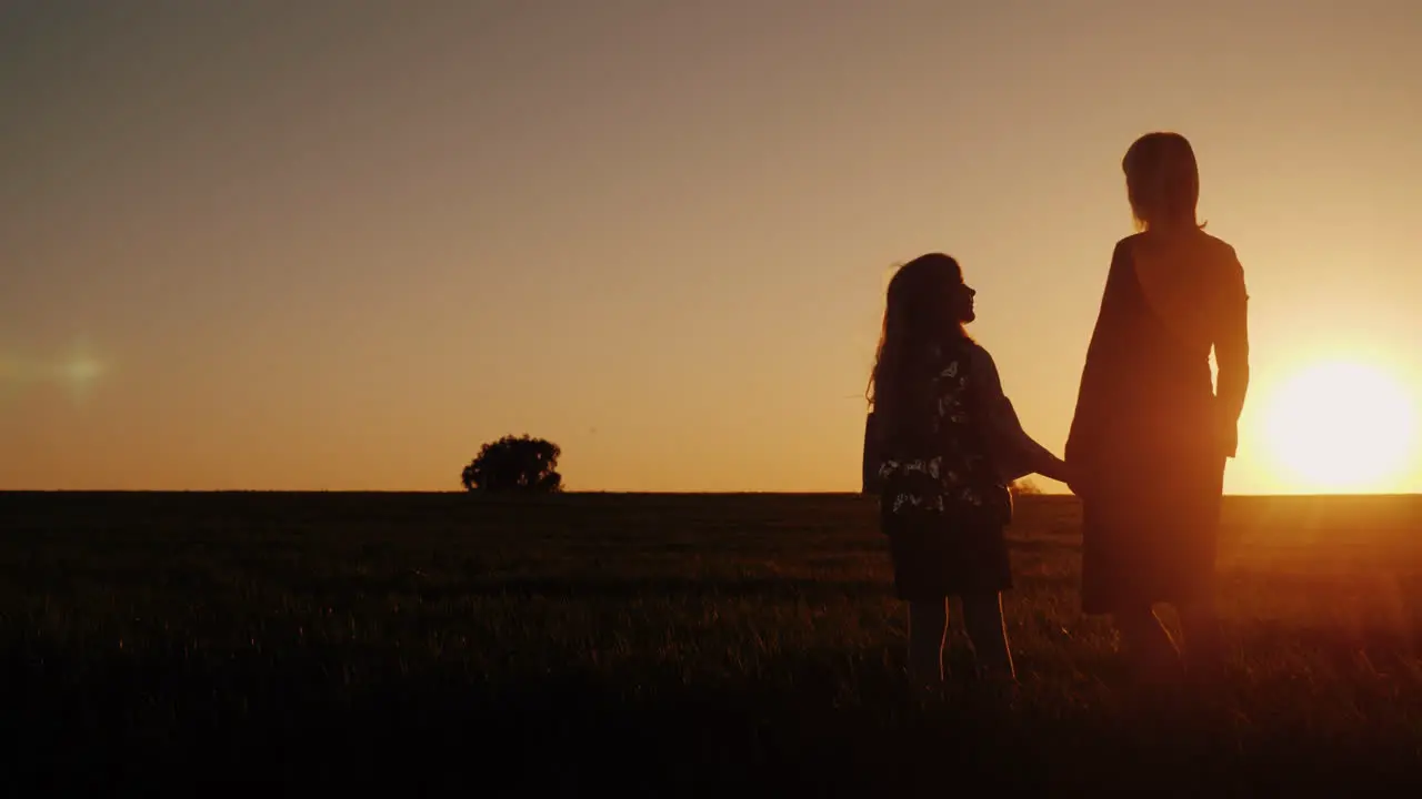 A Woman With A Girl Admires The Beautiful Sunset In A Picturesque Place Silhouettes Of Mom And Daugh