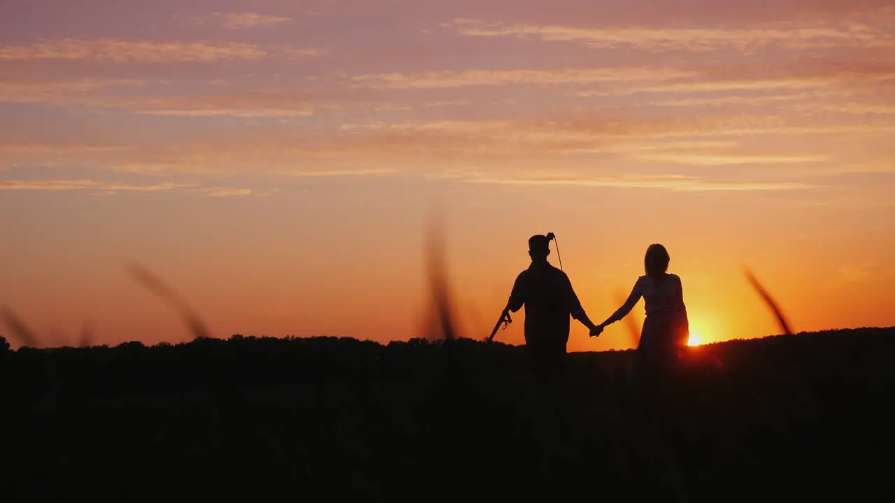 A Young Couple Of Farmers Walking Across The Field To Meet The Camera Silhouettes At Sunset 4K Video