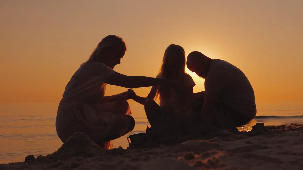 Parents Play With Daughter In The Sand Near The Sea Build Together A Sand Castle