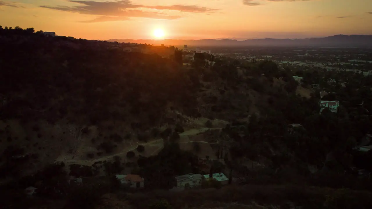 Flyover silhouetted hills reviewing a beautiful sunset over a hazy valley city