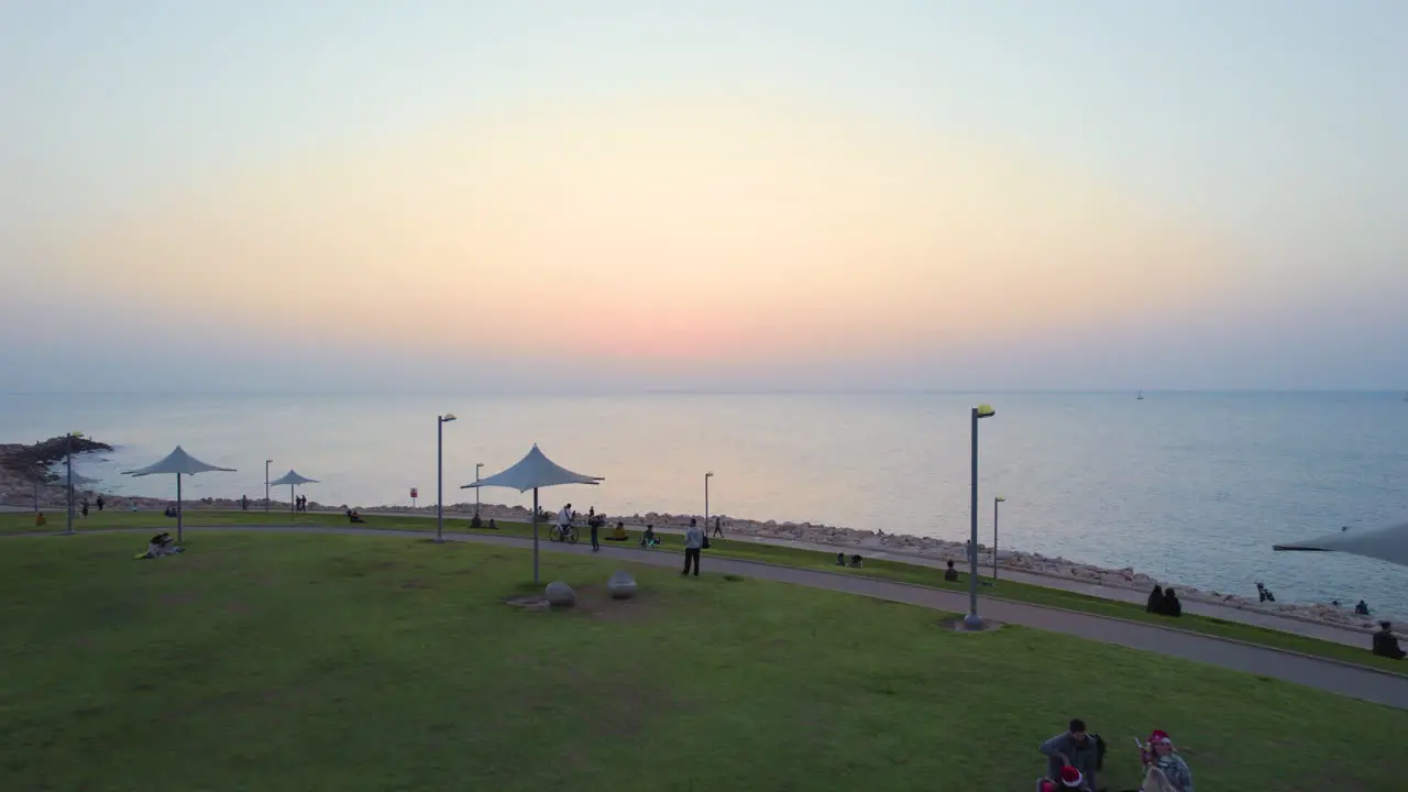 People relax on a grassy hill in front of the sea during a red sunset on Christmas week 22-23