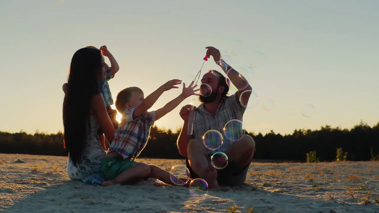 Young Parents And Two Sons Of The Family Playing With Soap Bubbles At Sunset