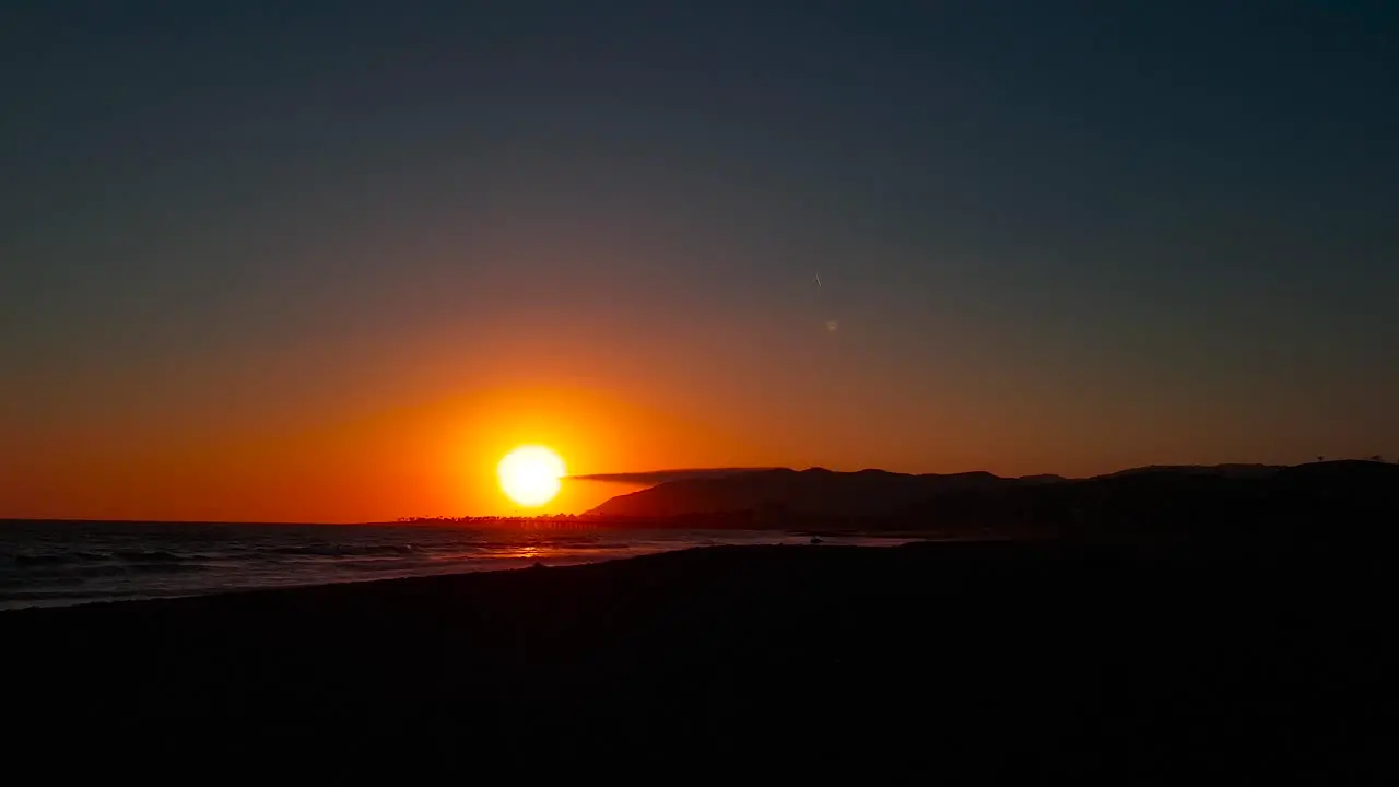 Slow panning shot of sunset by the beach with lone plane contrail in the sky at San Buenaventura State Beach in Ventura California United States