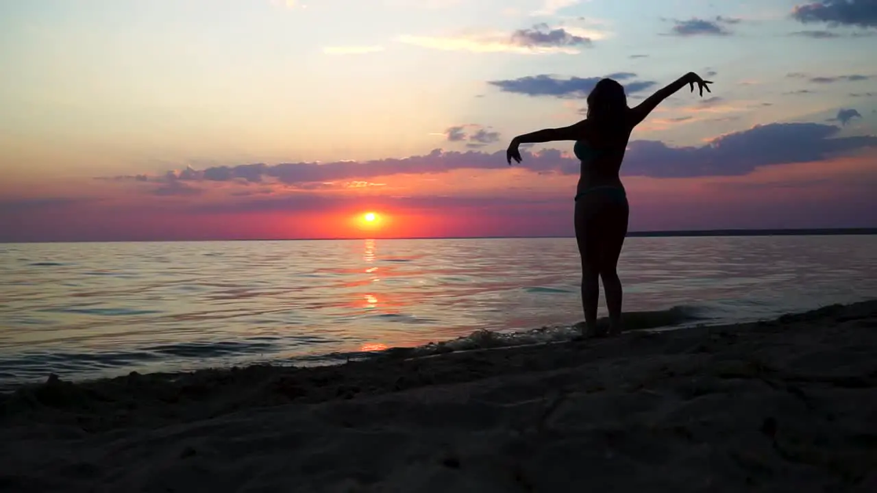 Dancing silhouette of girl in swimsuit in front of the sea at sunset