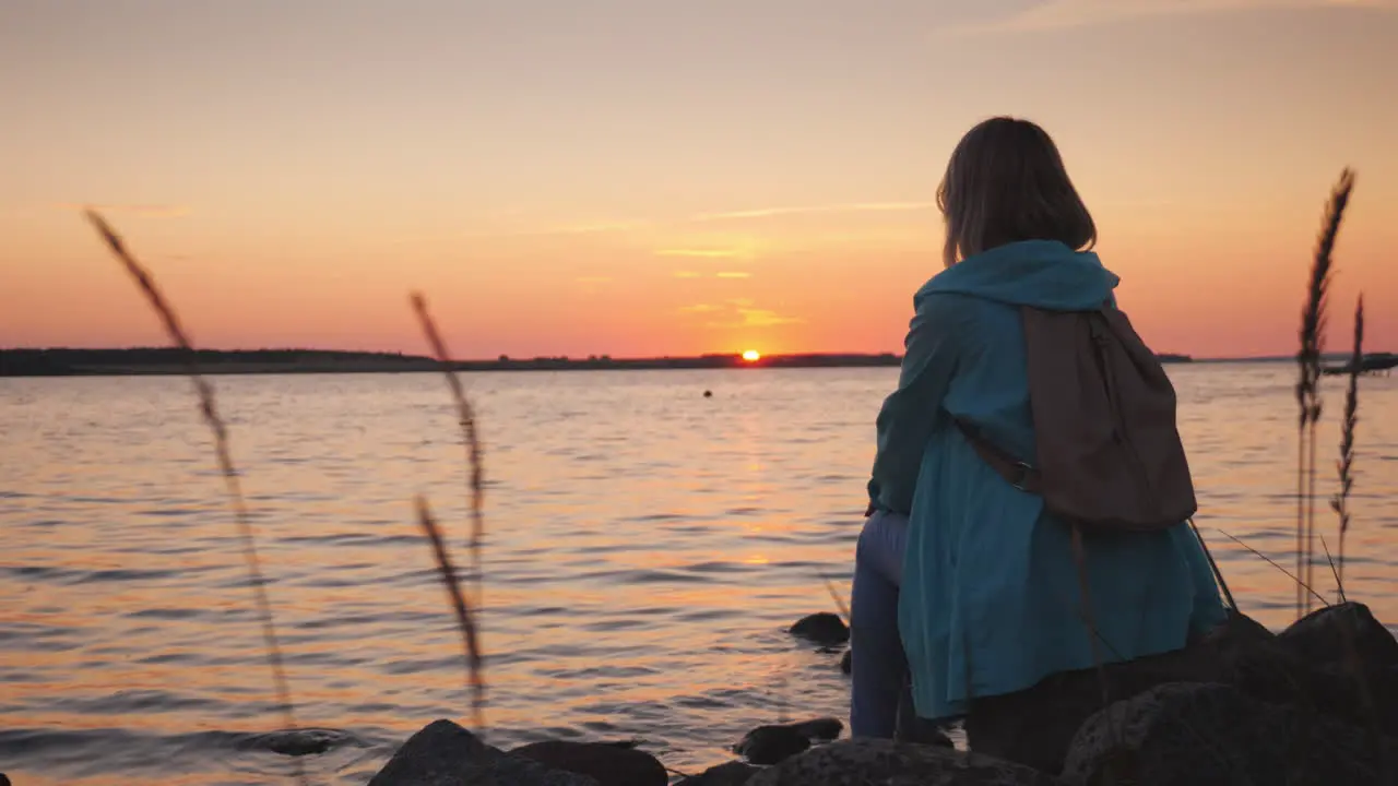 A Lonely Woman Sits On A Rock Near A Picturesque Lake At Sunset