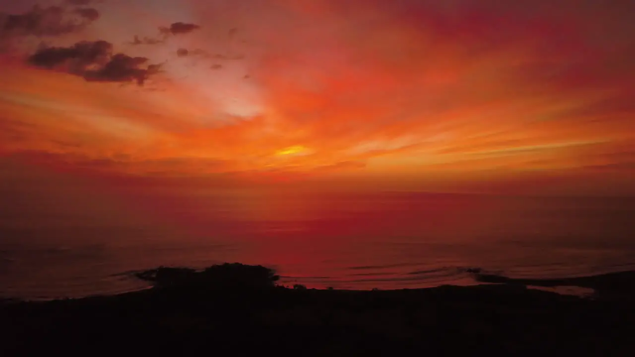 Cinematic aerial view of a vibrant red sunset over a tropical ocean