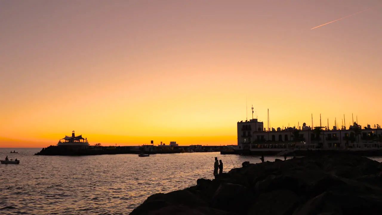 Fishermen on pier and coast during orange sunset casting fishing line on the open sea in the background is the city and harbor of sunset Grand Canary island valley 4k slow motion capture at 60fps