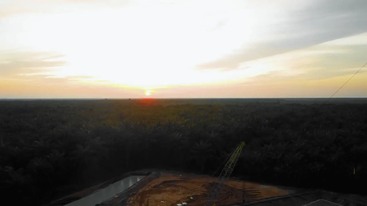 Cinematic 4K Drone Footage of Onshore Drilling Rig equipment structure for oil exploration and exploitation in the middle of jungle surrounded by palm oil trees during sunset and high oil price