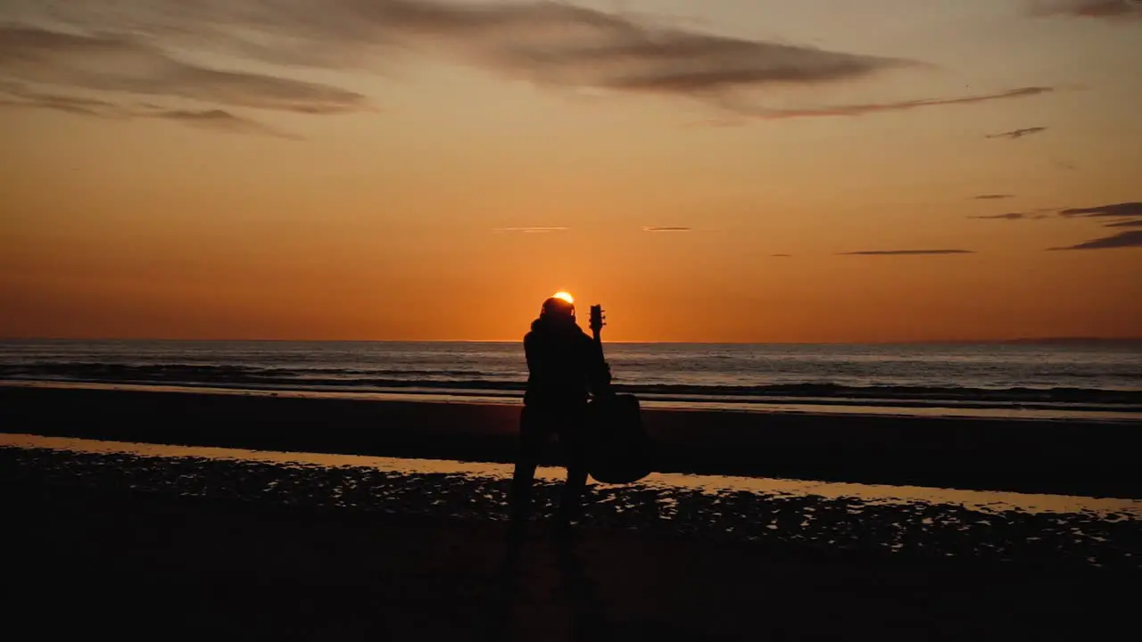 Man running with guitar in back sand beach at sunset-1