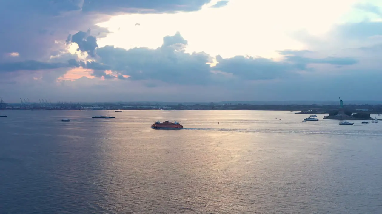 Aerial zoom towards Staten Island Ferry and the Statue of Liberty in the distance at dramatic sunset dusk