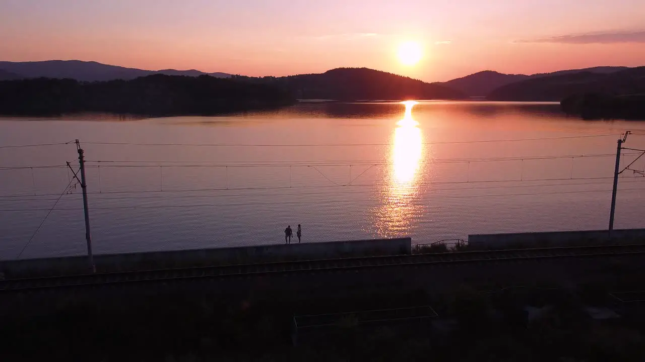 Aerial shot of walking couple railway track clear sky sunset and huge orange lake