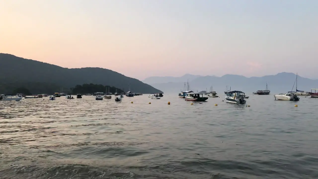 Boats bobbing in bay with sunset over mountains in background