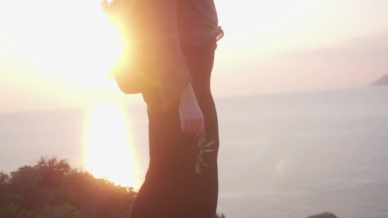 Female walks across hills by the sea with the sunset behind