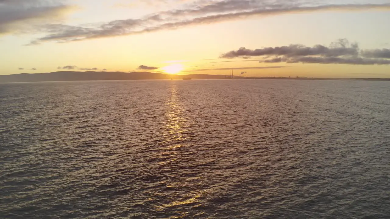 Aerial view over calm sea water as the sun sets on the horizon