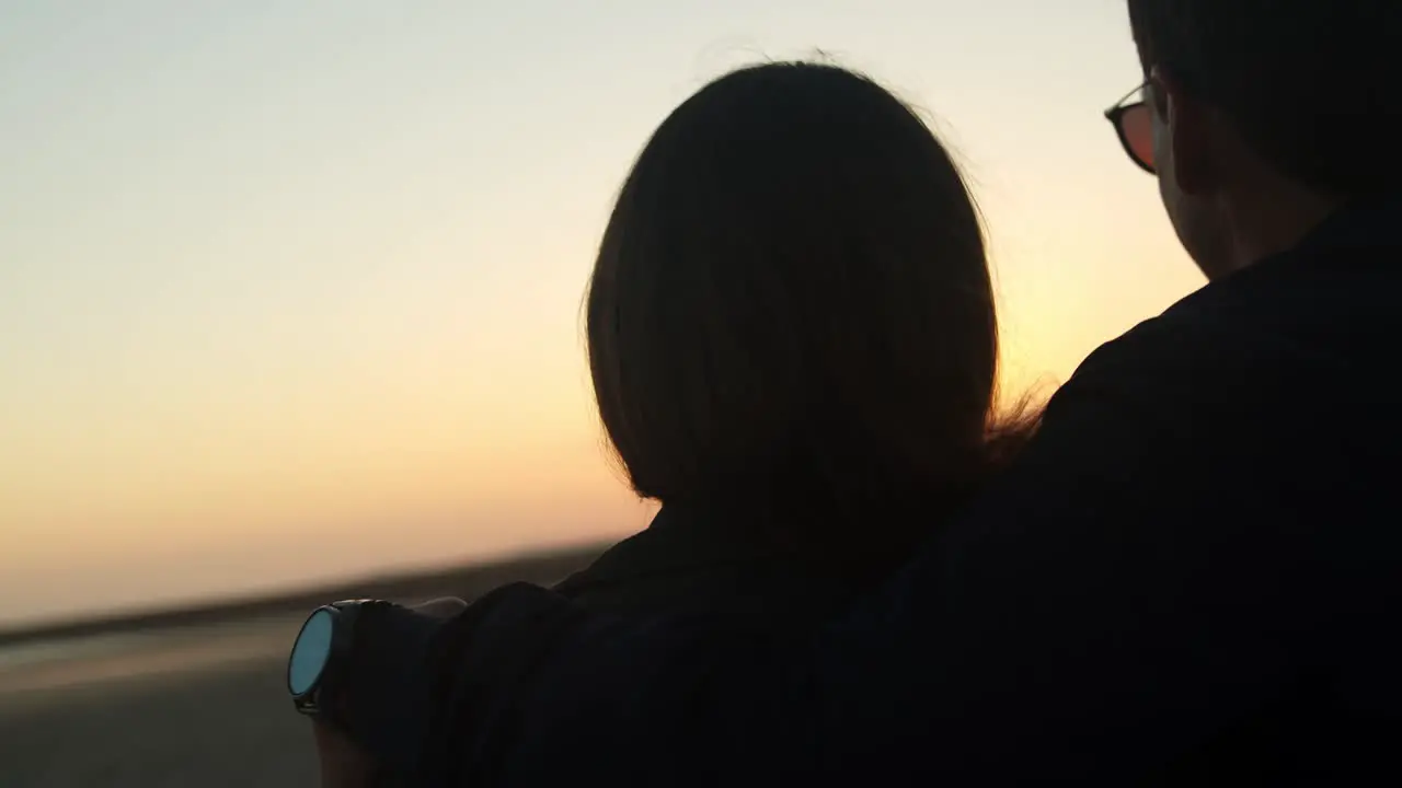 Couple watching the sunset and hugging at the beach handheld close up