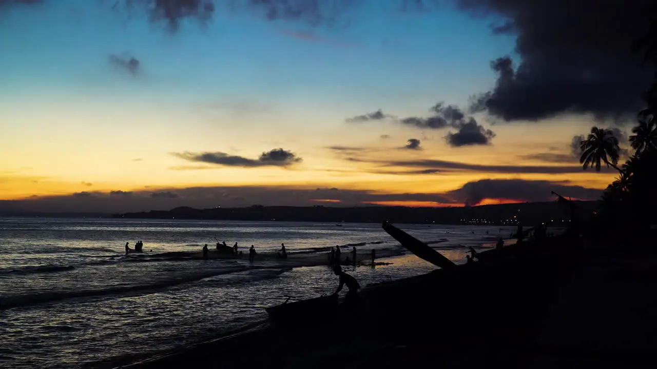 Silhouette men pulling out fishing net from ocean beach during sunset